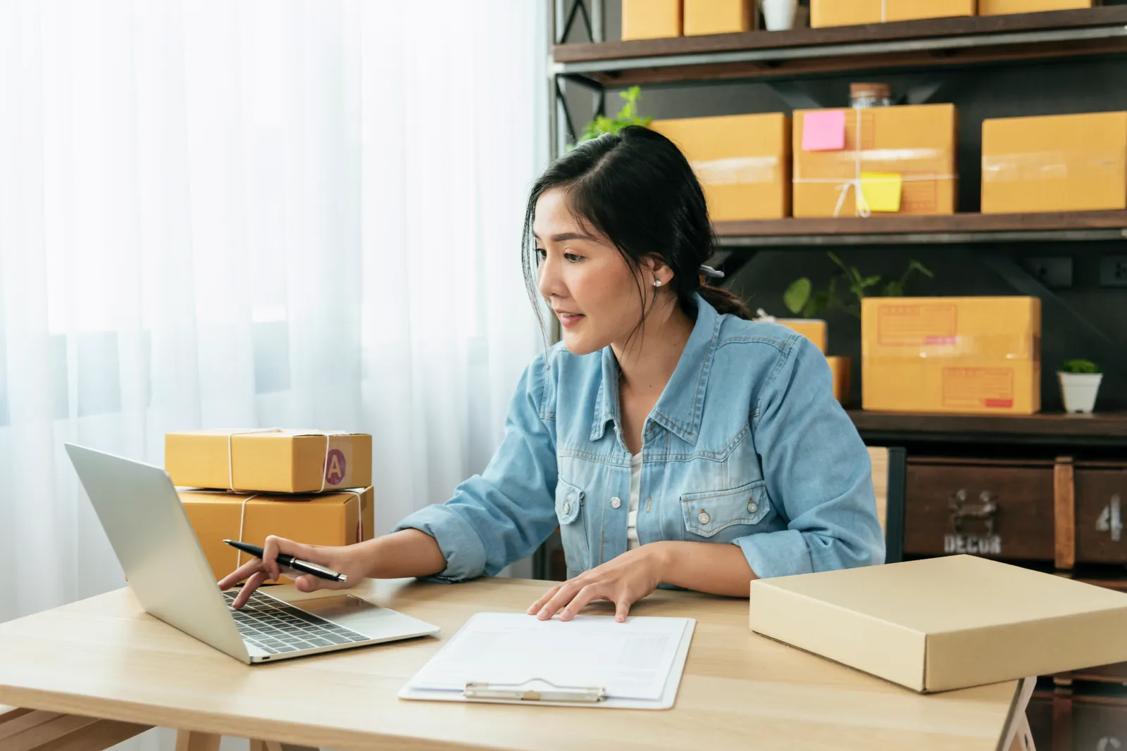 Shop owner processing online orders beside stacked shipping boxes