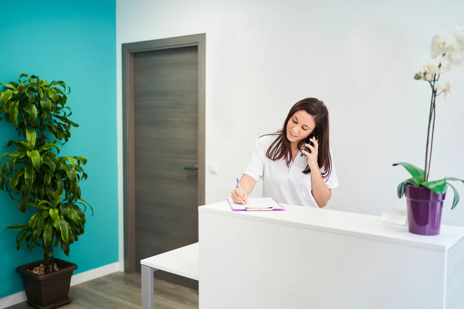 Clinic receptionist taking a booking call at the front desk
