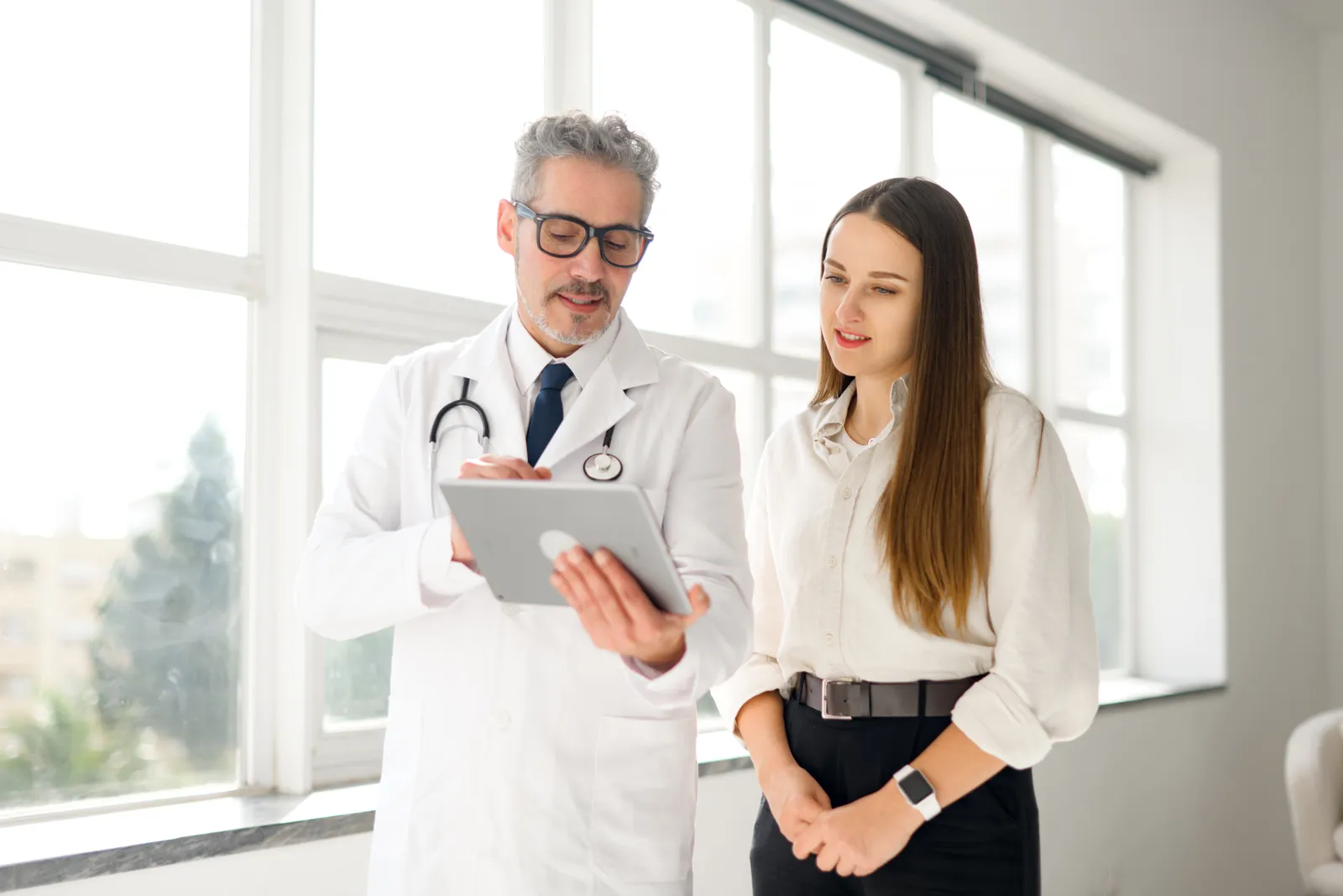 Doctor reviewing notes on a tablet with a patient in a bright clinic