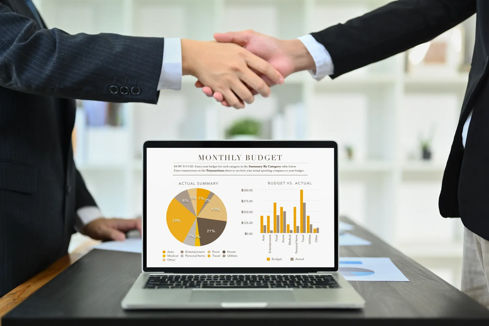 Handshake over a laptop showing a budget breakdown