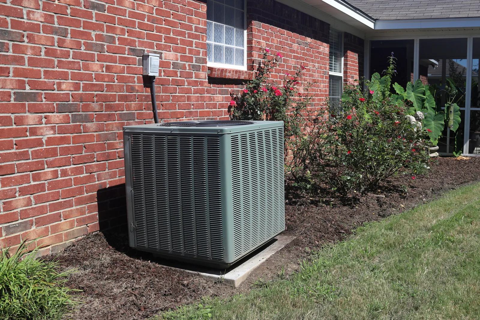 Residential air-conditioning condenser beside a brick home