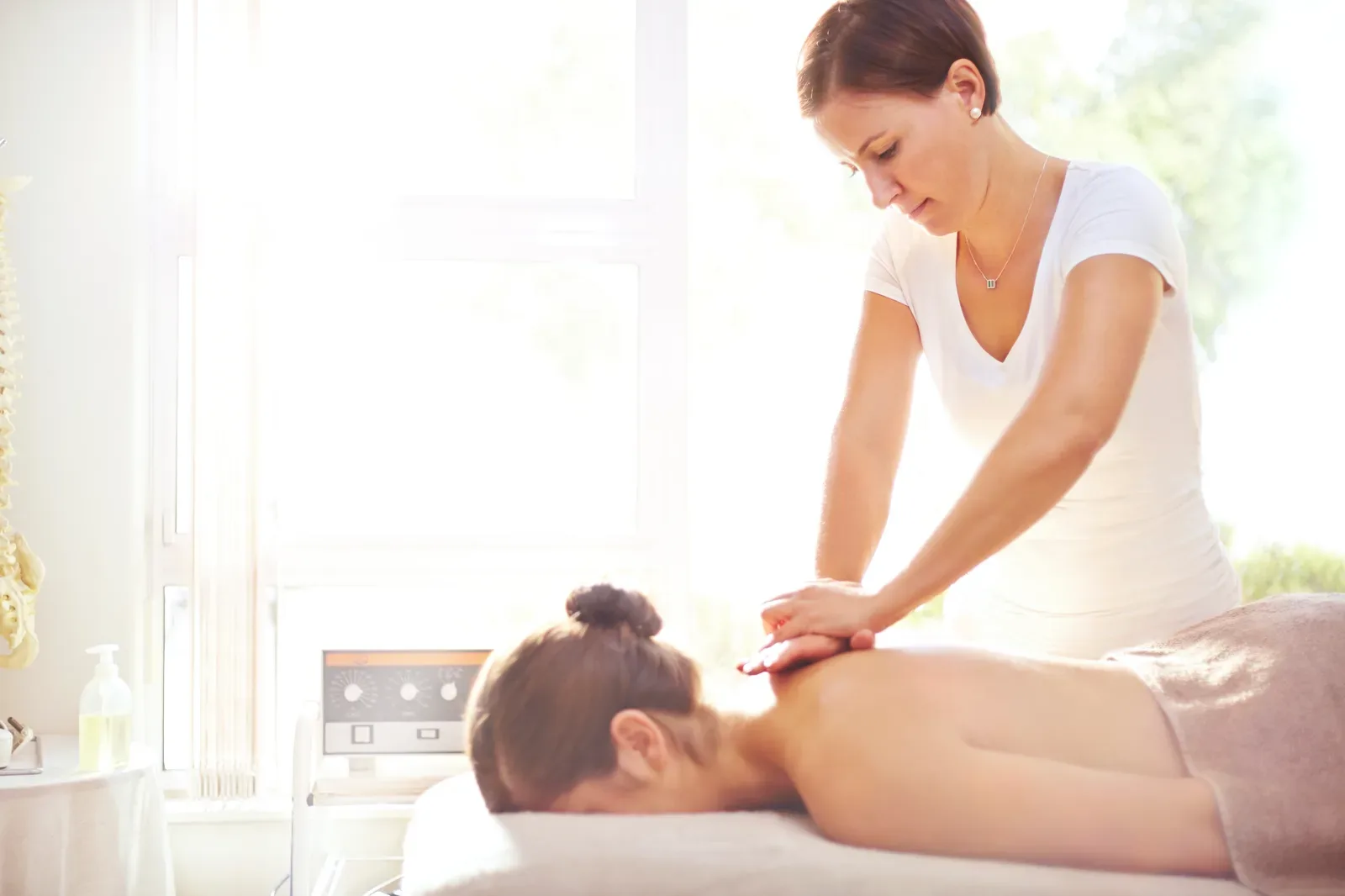 Massage therapist easing a client's shoulders in a softly lit day spa treatment room