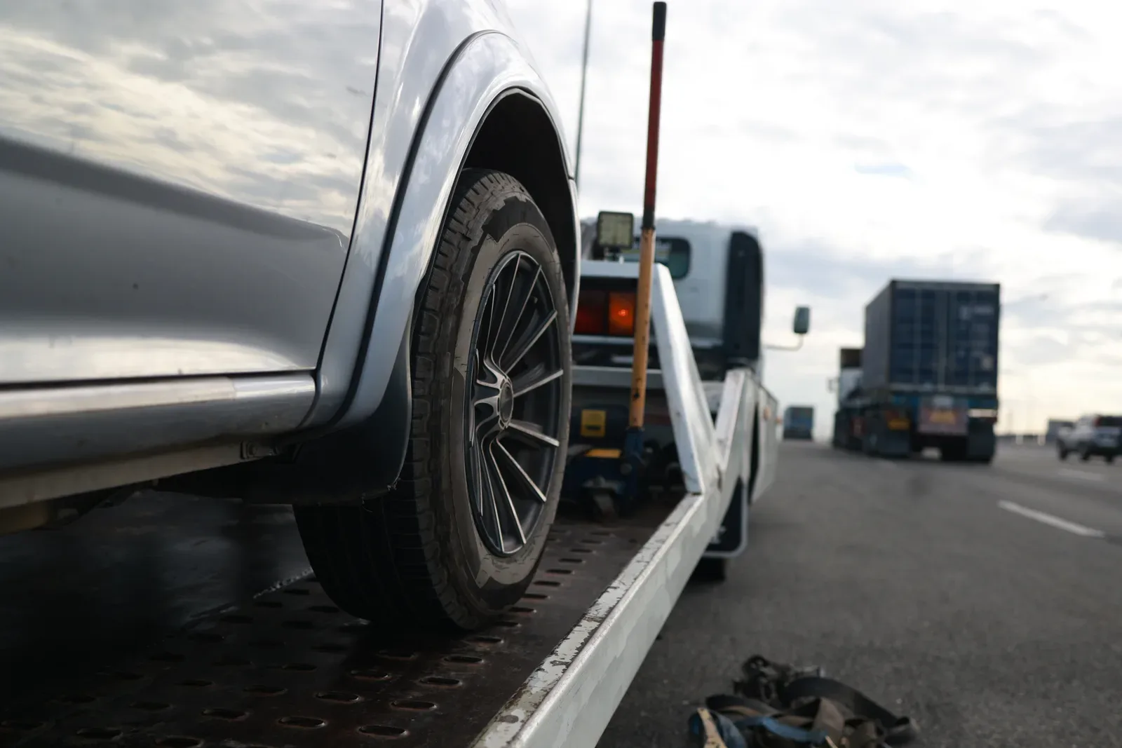 Tow truck operator winching a disabled sedan onto a flatbed at the roadside