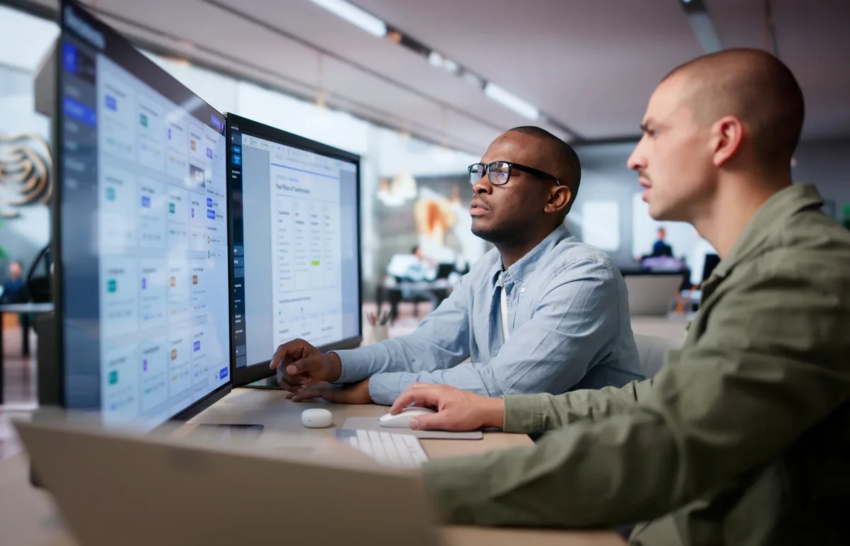 Two web developers reviewing a website layout and analytics on a large monitor, planning continuous improvements