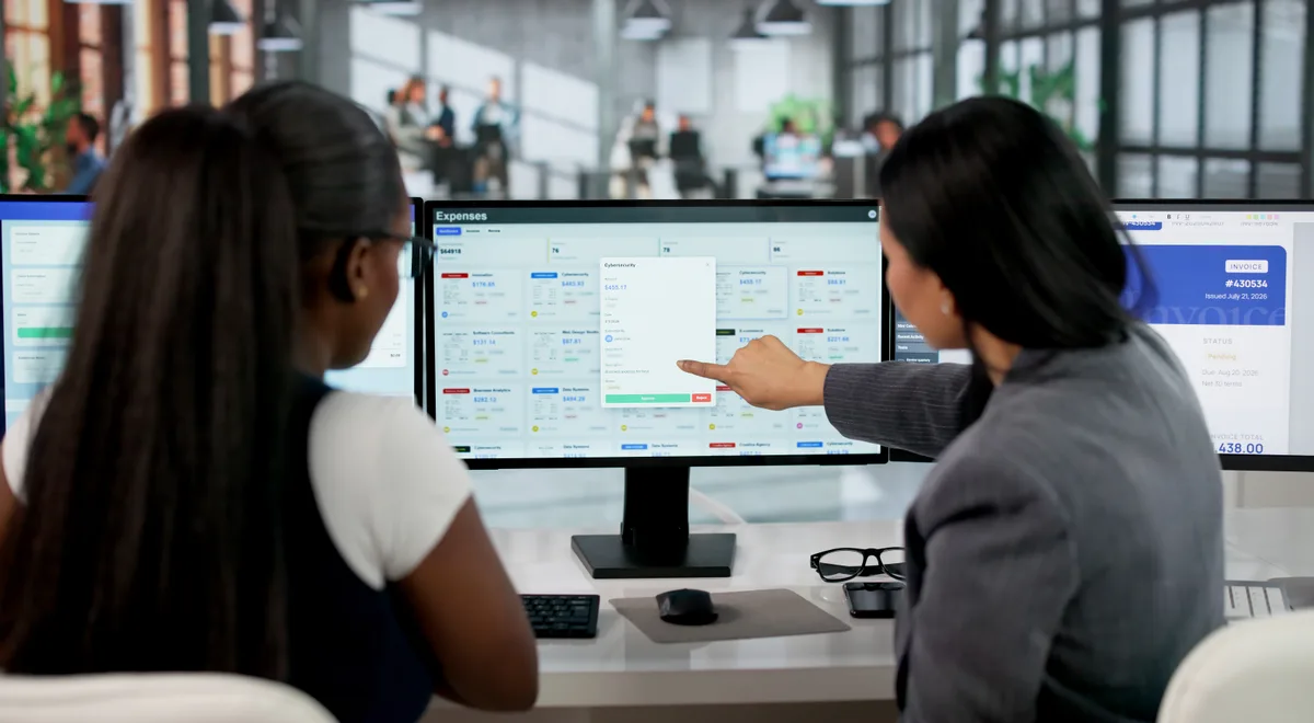 Two B2B colleagues reviewing a sales pipeline and lead-tracking dashboard on a desktop monitor in an office