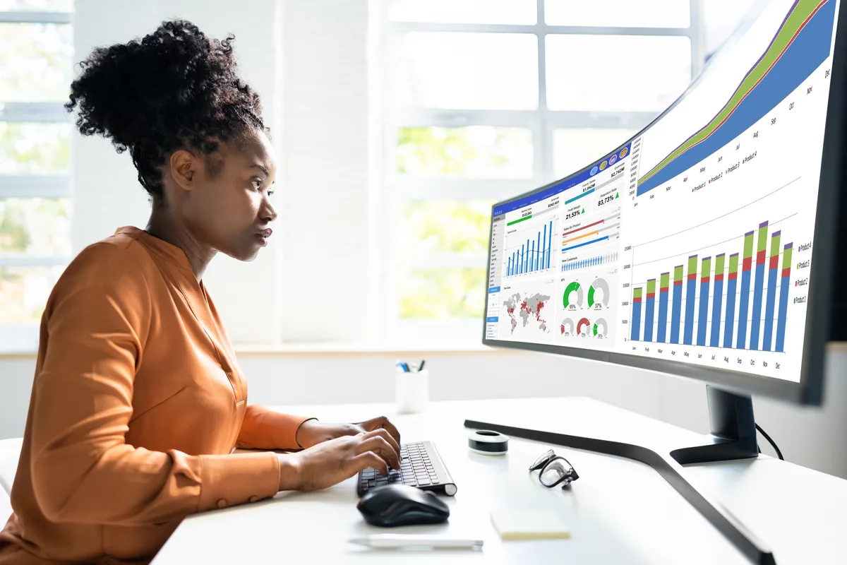 A marketing analyst reviewing a combined performance dashboard showing ad, CRM, and revenue data on a widescreen monitor
