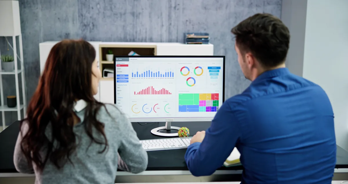 Two marketing analysts reviewing GA4 reports and tracking tags on a desktop monitor in a modern office