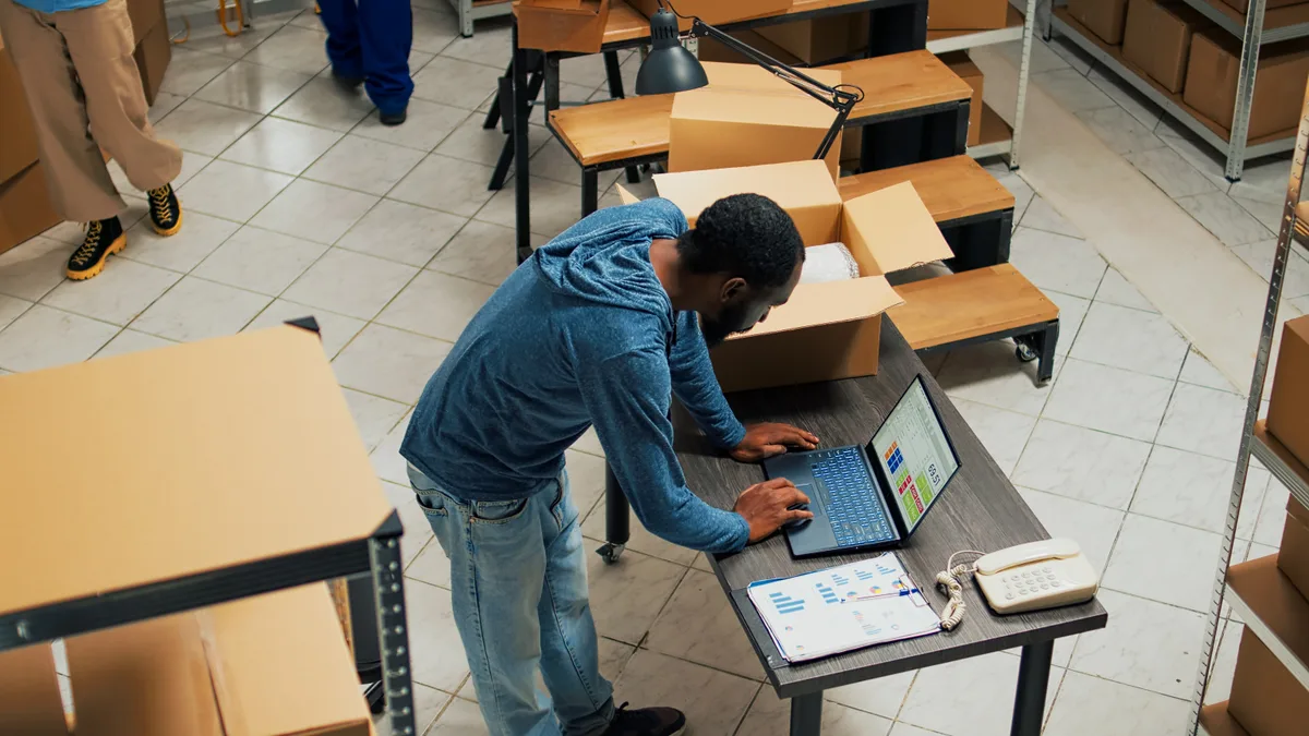 An e-commerce manager reviewing product profit margins and ad performance on a laptop in a warehouse office