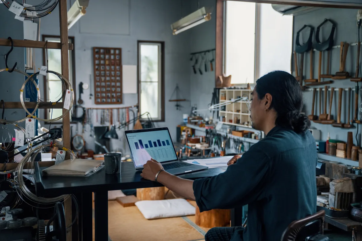 E-commerce store owner reviewing profit margins and ad spend on a laptop in a product workshop