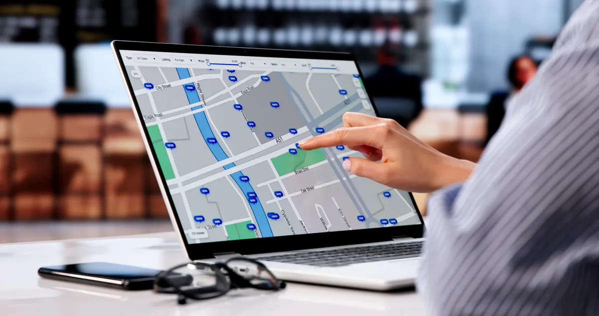Small business owner planning regional expansion while reviewing a map of nearby cities on a laptop