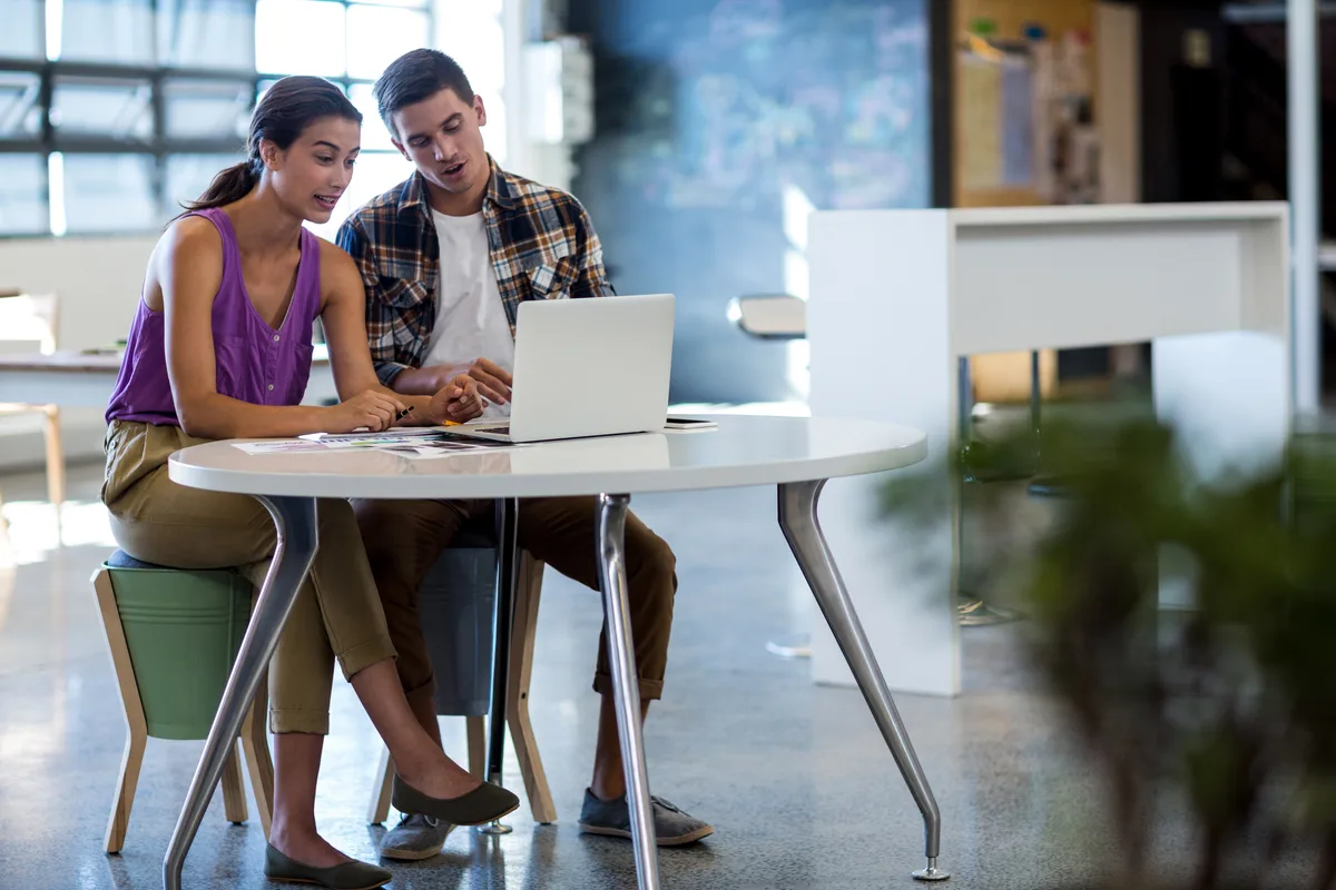Two e-commerce specialists reviewing a product catalogue and URL list on a laptop while planning a platform migration