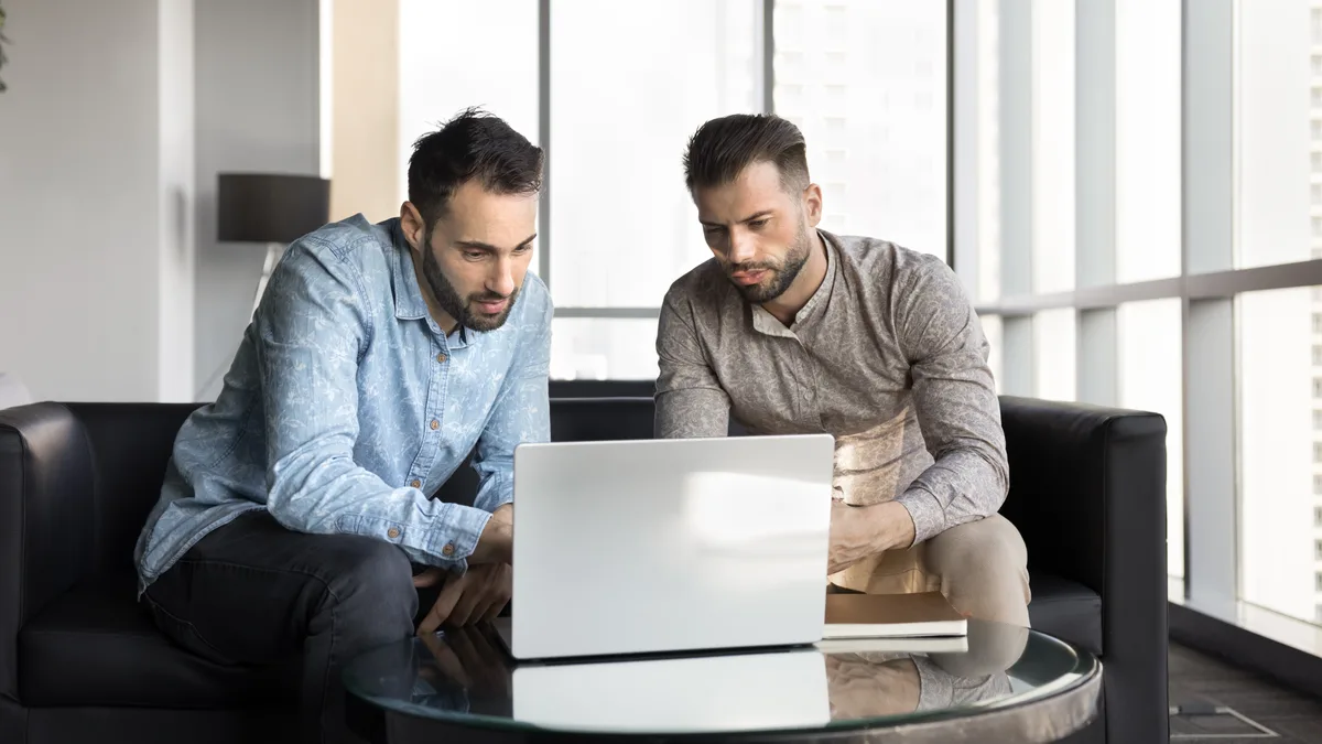 A business owner and a developer reviewing a software development contract and source code on a laptop