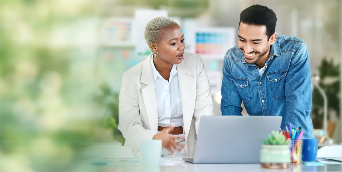 Two colleagues at a desk reviewing a marketing campaign timeline and performance metrics on a laptop screen