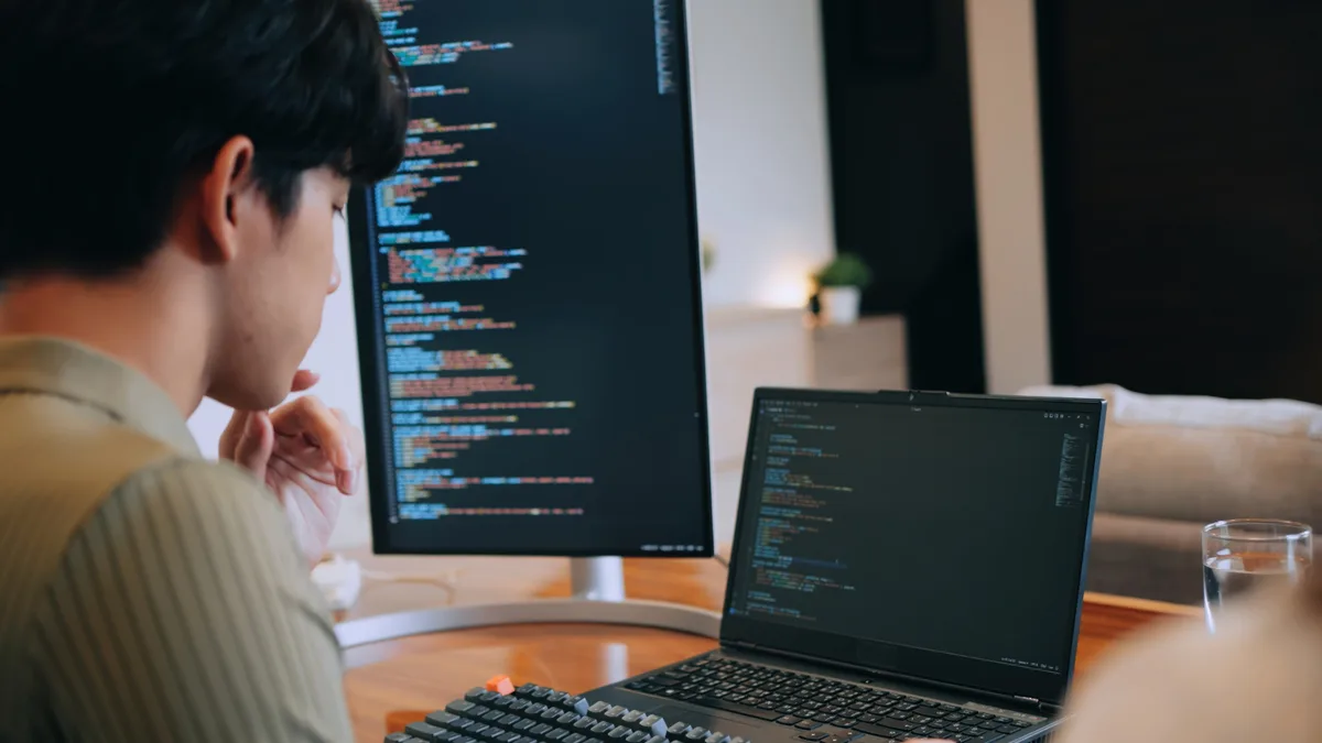 Two developers reviewing a database schema and dashboard on dual monitors while planning a custom CRM build