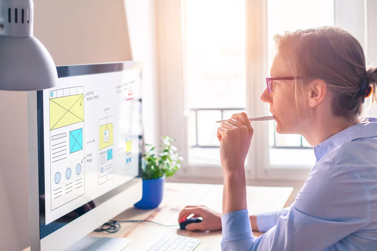 A web designer reviewing a landing page layout and wireframe on a large desktop monitor in a bright studio