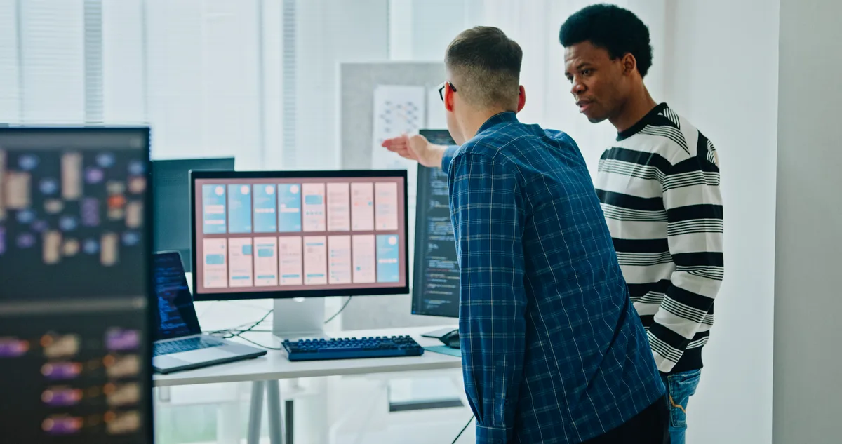 Two developers reviewing a customer portal dashboard layout on a desktop monitor in a Canadian office