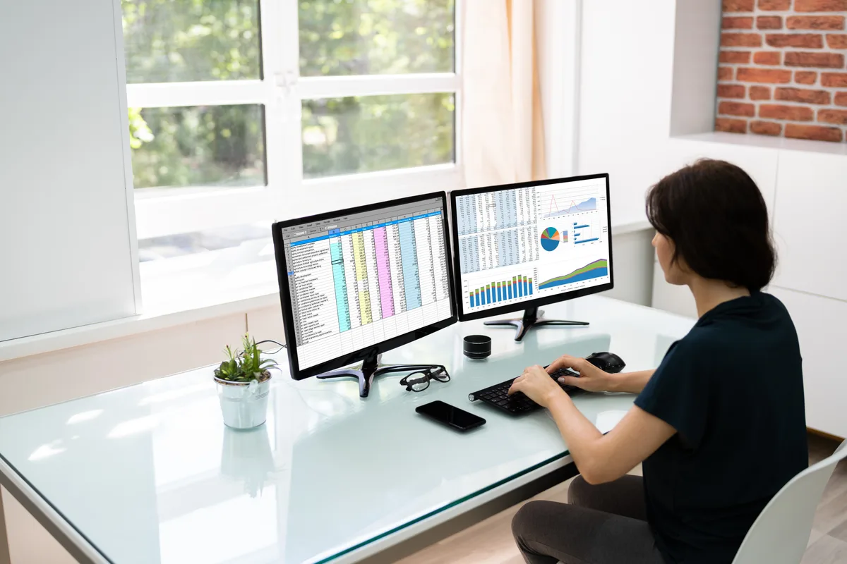 A digital marketing analyst reviewing Google Ads conversion reports across two monitors to find duplicate tracking
