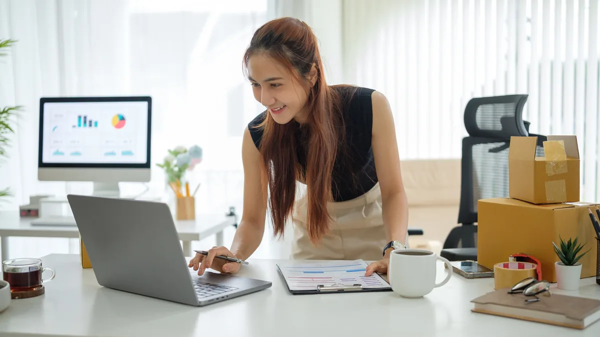 E-commerce store owner reviewing product sales data on a laptop beside packed inventory