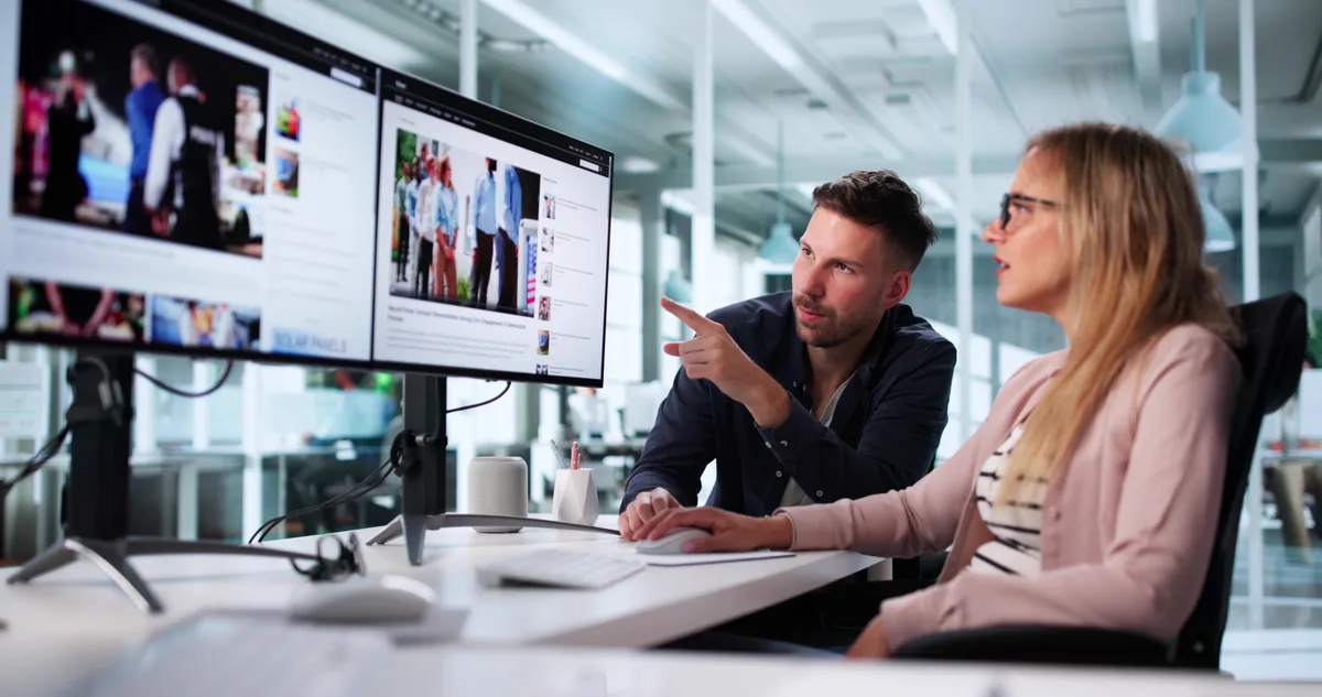 Two designers reviewing a website layout on a large monitor while deciding whether to redesign or refine it