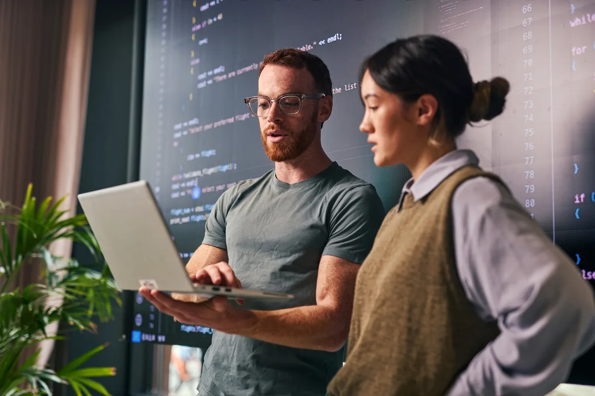 Two developers reviewing a custom application's code on a monitor while planning a build