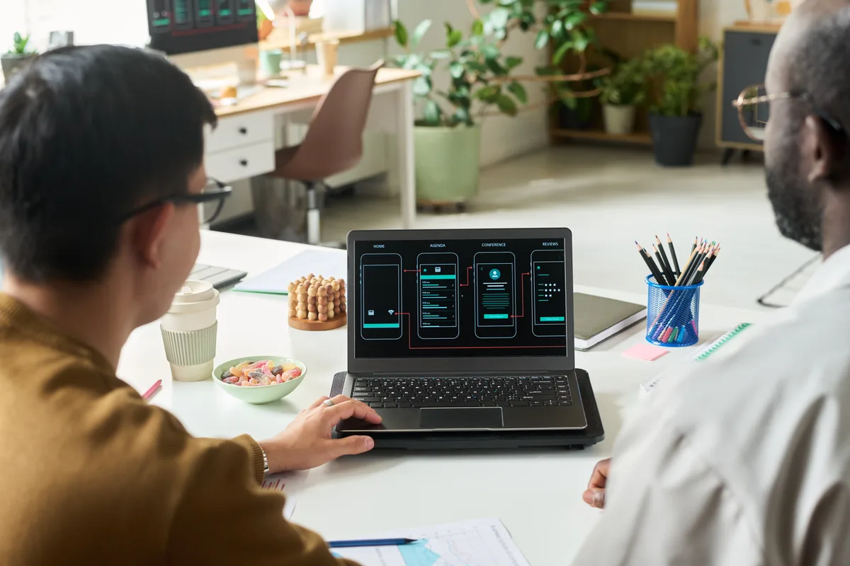 A web designer and client reviewing wireframes and a redesign scope document on a laptop together