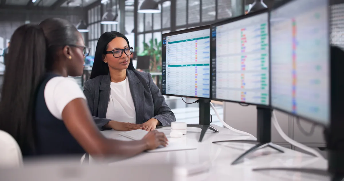 Two marketers comparing Google Ads and GA4 conversion reports side by side on separate monitors