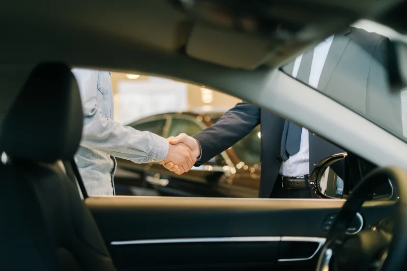 A customer and an Atlantic Motors product advisor shaking hands through the open window of a new vehicle