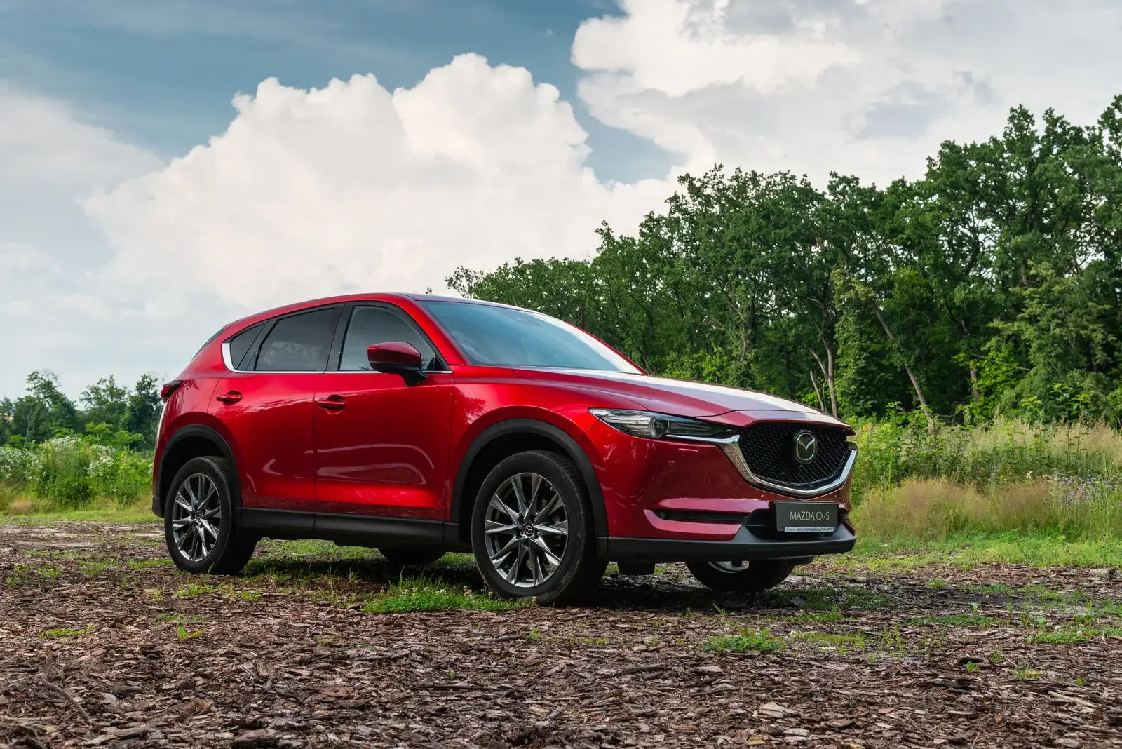 Soul red Mazda CX-5 GT parked at the edge of a wooded clearing