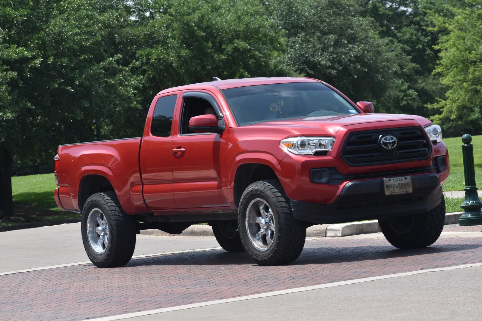 Lifted red Toyota Tacoma SR5 on all-terrain tires crossing a park roadway