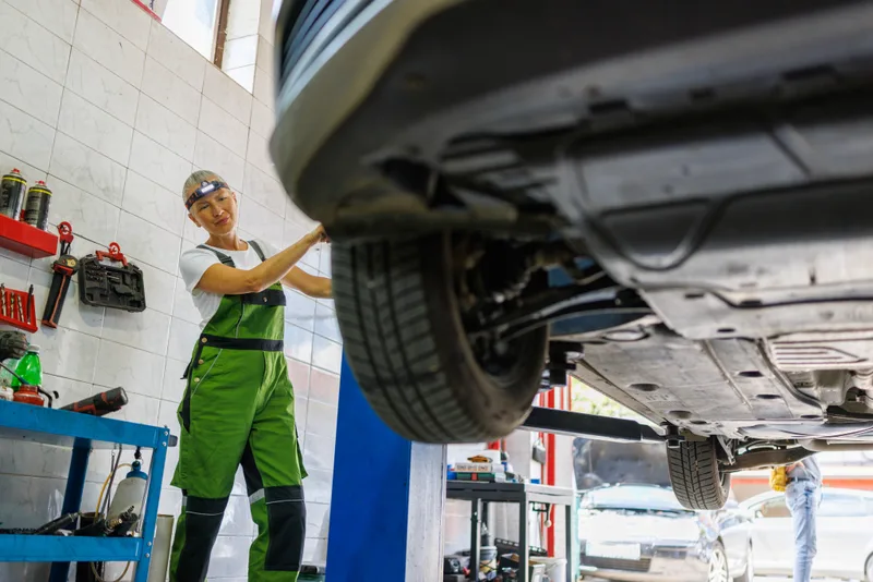 A licensed technician inspecting the underside of a vehicle on a hoist in the Atlantic Motors service bay