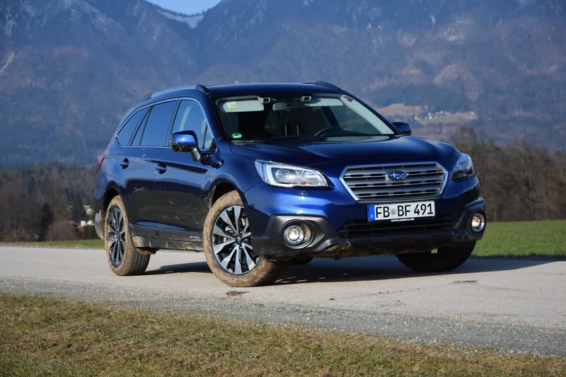 Blue Subaru Outback 3.6R parked on a gravel road with mountains behind