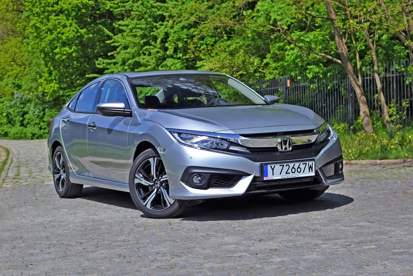 Silver Honda Civic Touring sedan parked on a tree-lined cobblestone lane