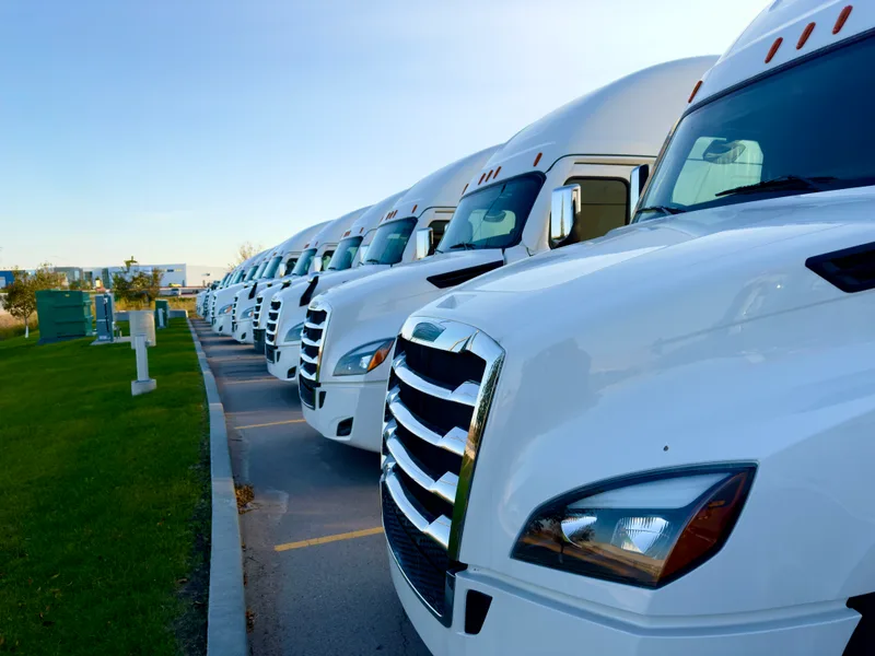 A row of white semi tractors parked nose to tail in a fleet yard at sunrise