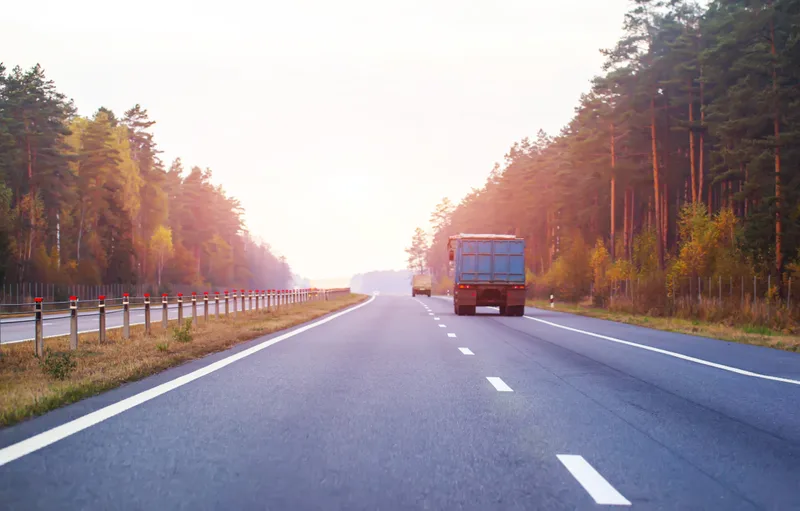 A truck on a two-lane highway between autumn trees