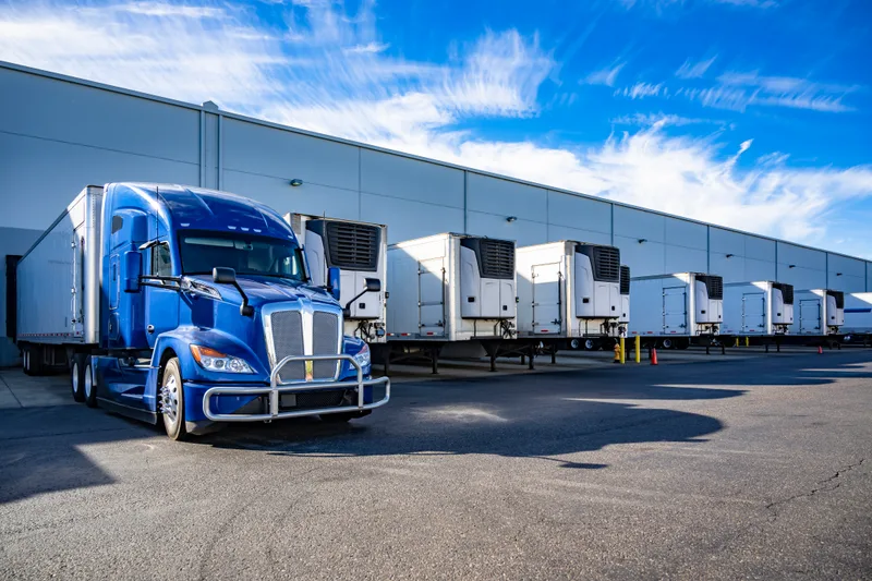 A blue semi tractor and refrigerated trailers lined up at a distribution center
