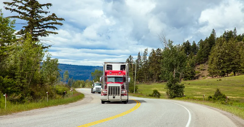 A red semi truck on a winding two-lane road