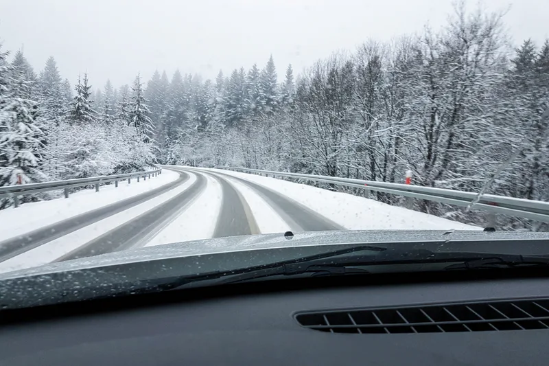 A snow-covered highway seen through a truck windshield