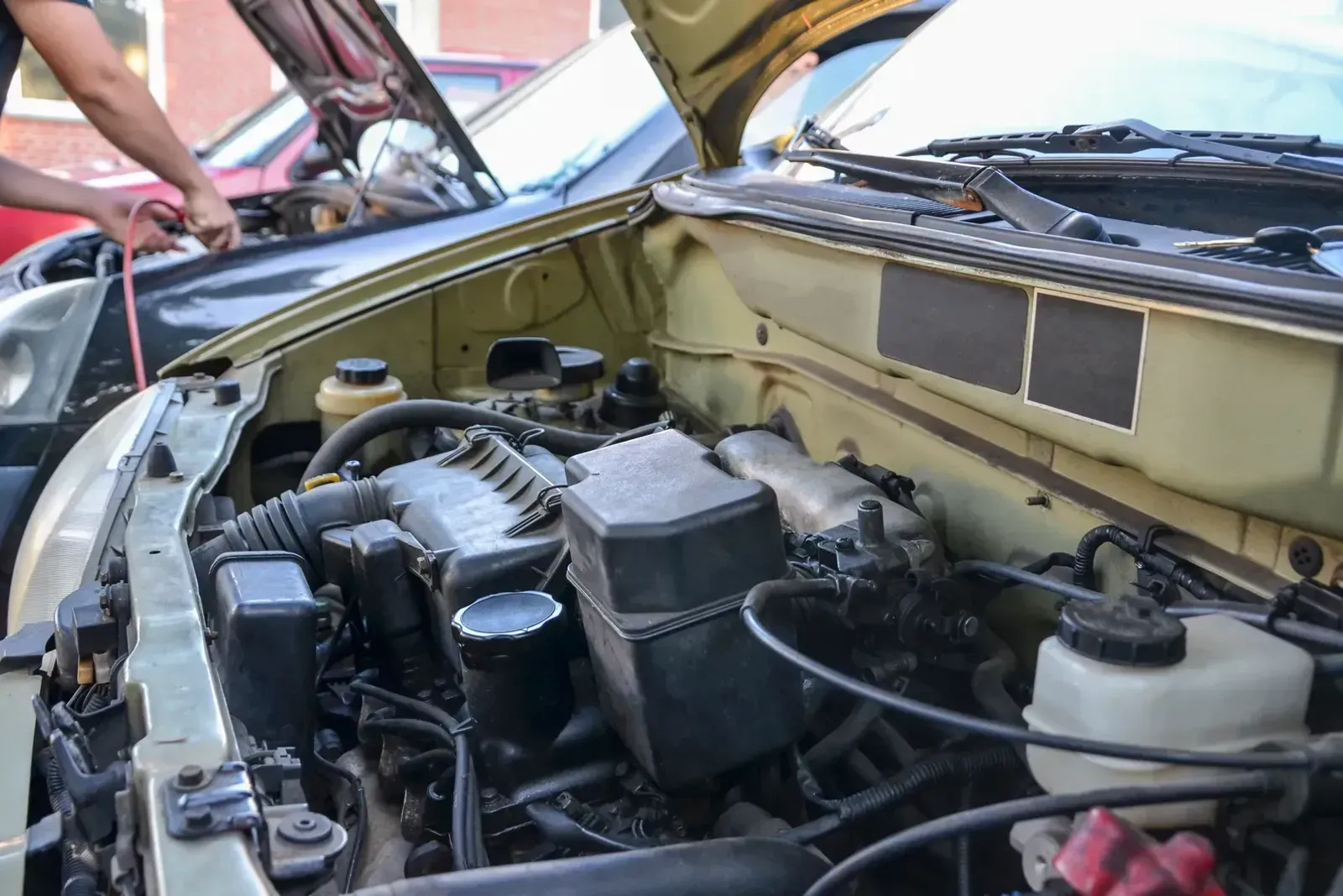 Technician clamping jumper cables onto the battery of a car with its hood raised at the roadside