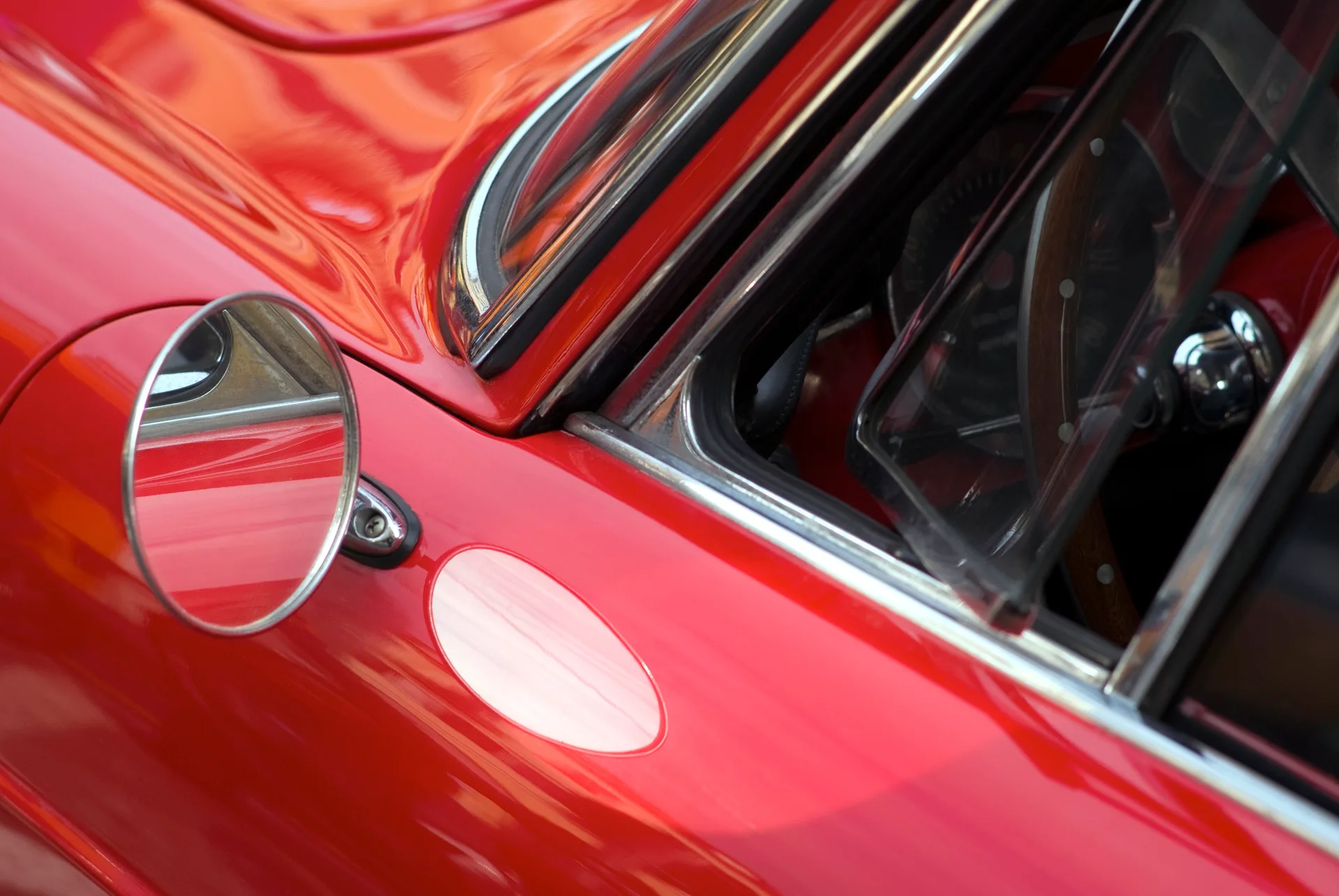 Close-up of a restored classic sports car in red — chrome wing mirror, polished quarter-window trim and deep paintwork