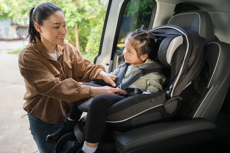 A parent buckling a toddler into a car seat in the back of a family SUV