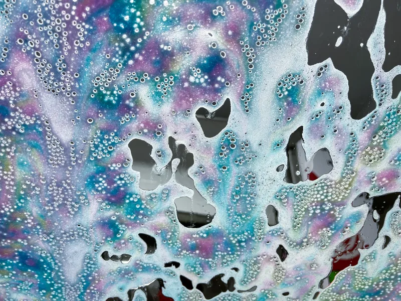 Blue, pink and white triple foam sliding down a windshield, seen from inside the car