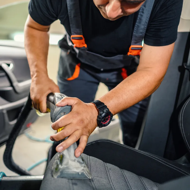 A worker vacuuming the front seat of a car with a wide nozzle