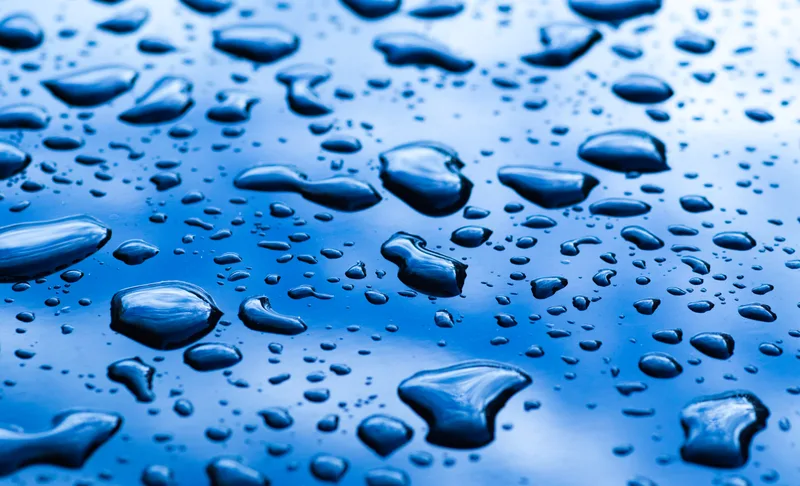 Tight round water beads sitting on glossy blue paint