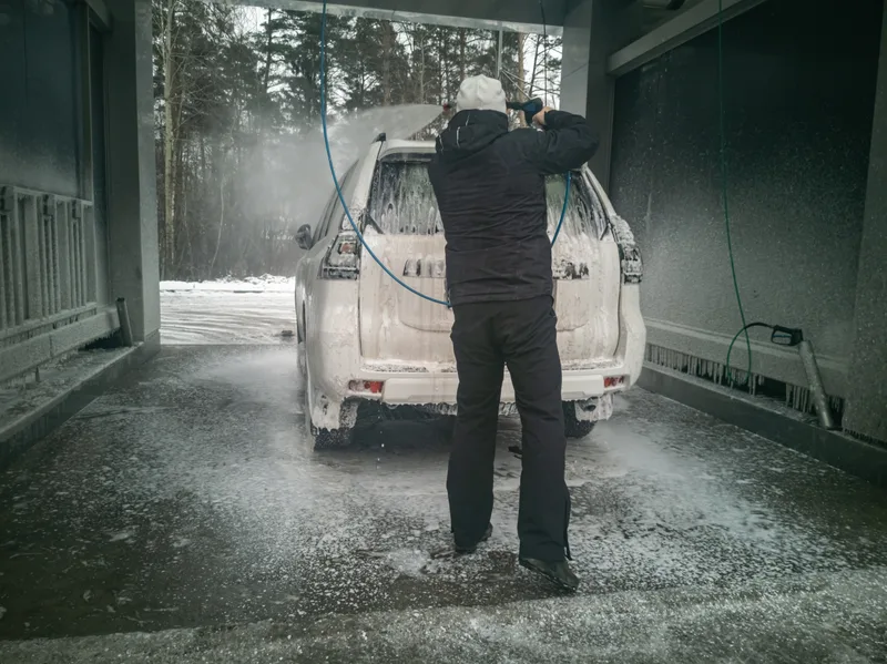 A driver pressure-washing road grime off an SUV in a wash bay on a snowy day