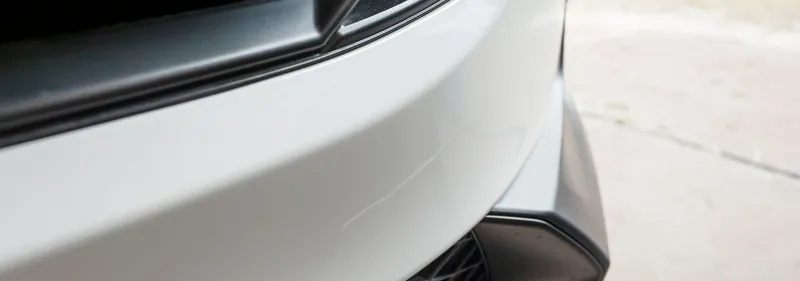 White car front bumper with a light scratch across the paint, before polishing