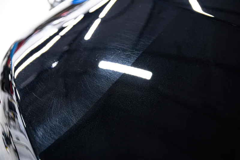 Black car hood split by a tape line, swirl marks on the left half and a clear mirror finish on the right
