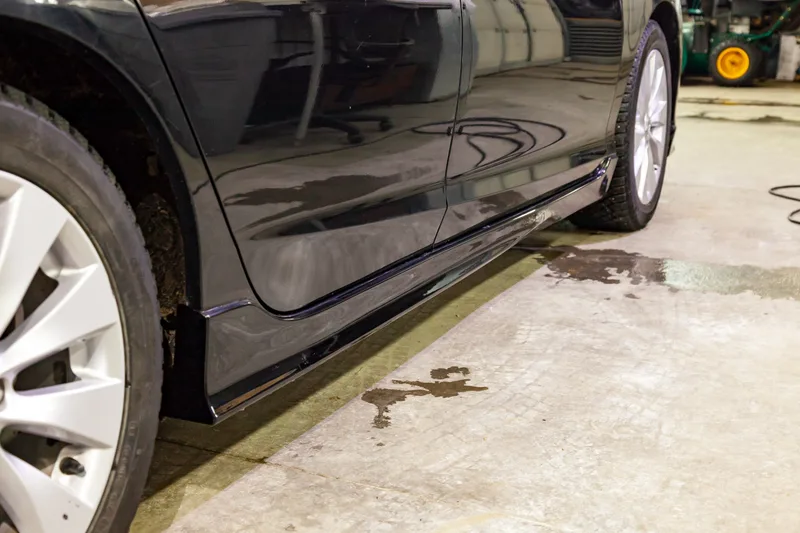 Side skirt of a black sedan in a detail bay, the front section polished and the rear section still dull
