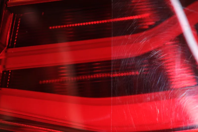 Red tail lamp lens with the left half polished clear and the right half covered in fine scratches