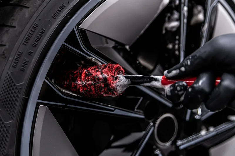 Detailer cleaning the inside of a black alloy wheel with a soft red wheel brush