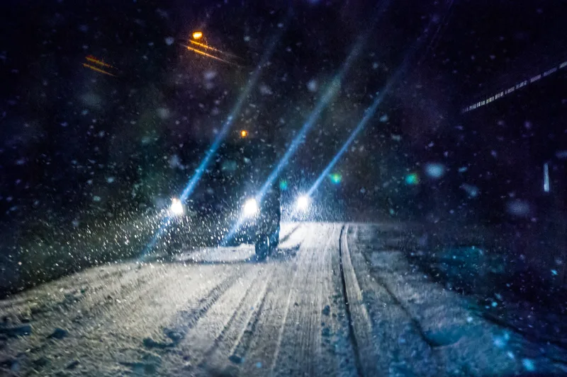 Headlights of a car driving through a snowstorm at night on a snow-covered road